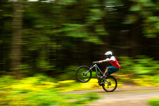 African American man mountain biking in a lush forest. Male biking for recreation. He is living an active lifestyle.