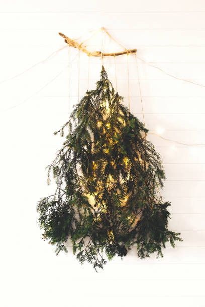 istock Alternative eco christmas tree concept. Modern christmas tree made of pine branches with golden festive lights hanging on white wooden wall. Scandinavian minimal decor in stylish room 1177574144