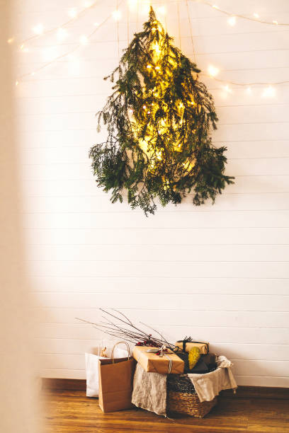 istock Stylish christmas gift boxes on wooden floor under creative christmas tree. Modern christmas eco tree of pine branches hanging on wall with festive lights and presents in rustic basket 1177574887