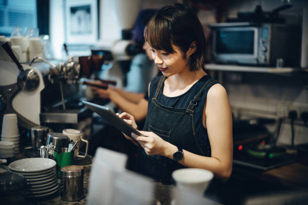 istock Young Asian female barista using a digital tablet while working behind a bar counter in a a coffee shop 1177590335