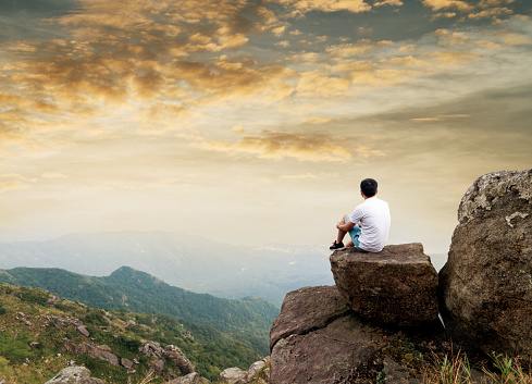 Man sitting on the top of mountain at sunset.