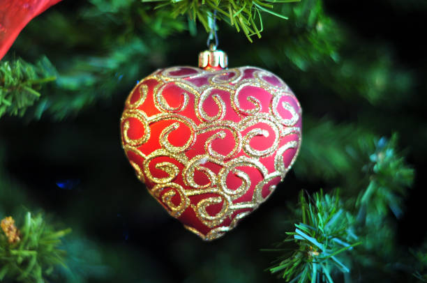 istock Pretty red heart shaped festive with gold swirl patterns hanging from artificial Christmas tree 1177598686