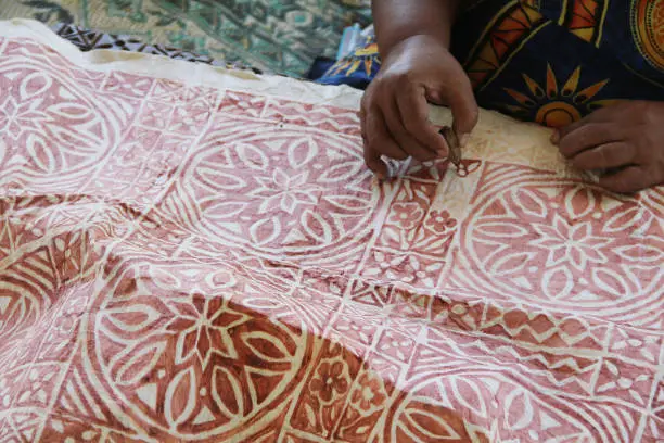 Photo of A Samoan lady drawing traditional pattern with mud water on a handmade mulberry paper.