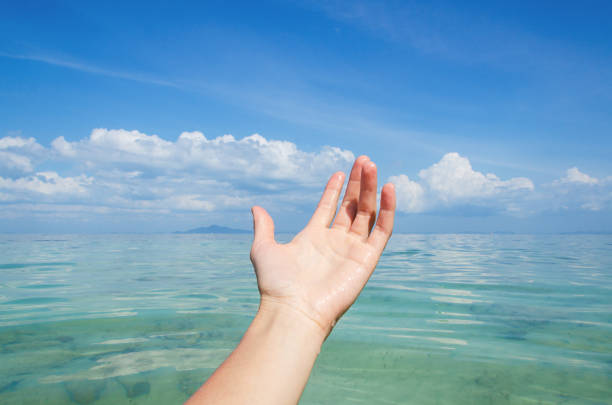 Female hand against tropical ocean and blue sky with beautiful clouds
