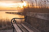 Autumnal sunset at the lake. Lakeshore with a bench and wooden walkway.