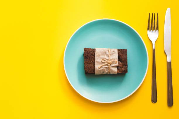 Appetizing fresh cooked brownie on colored plate with knife and fork and yellow background with copy space. Top view.