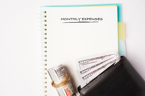Money management concept. Monthly expenses wordings on notebook with wallet and money