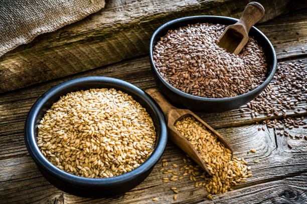 Dietary fiber: black bowls filled with organic flax seeds shot on rustic wooden table. One bowl contains brown flax seeds at the other contains golden flax seeds. Predominant colors are brown and gold. XXXL 42Mp studio photo taken with SONY A7rII and Zeiss Batis 40mm F2.0 CF