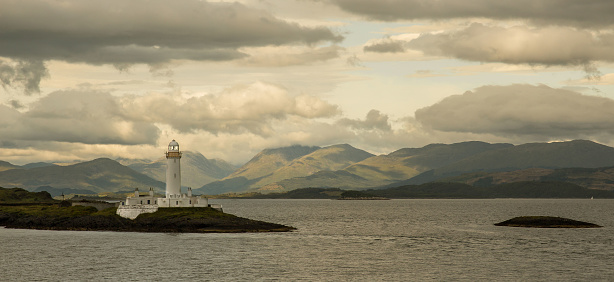 Eilean Musdile Lighthouse with clouds in the sky, in the West Coast of Scotland, seen from the ferry from Oban to Craignure, in the Isle of Mull. Seascape. UK