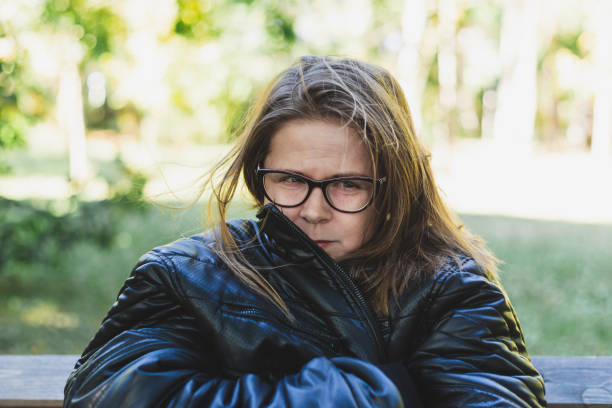 Beautiful young woman with leather jacket feeling cold outdoors - Casually dressed pretty girl with brown hair wearing eyeglasses freezing in the park - Attractive female trembling in nature
