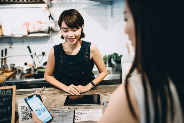 istock Customer scanning QR code, making a quick and easy contactless payment with her smartphone in a cafe in front of a smiling barista 1177644571