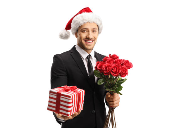 istock Young elegant man wearing a suit and a Santa hat holding roses and a present 1177646326