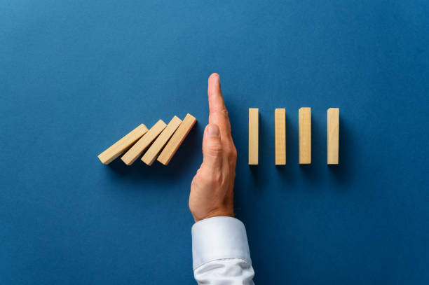 View from above of male hand interfering collapsing dominos View from above of male hand interfering collapsing dominos in a conceptual image of business crisis management. Over navy blue background. domino stock pictures, royalty-free photos & images