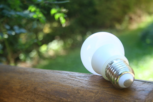 LED bulb on the wooden table with green nature background for eco saving concept