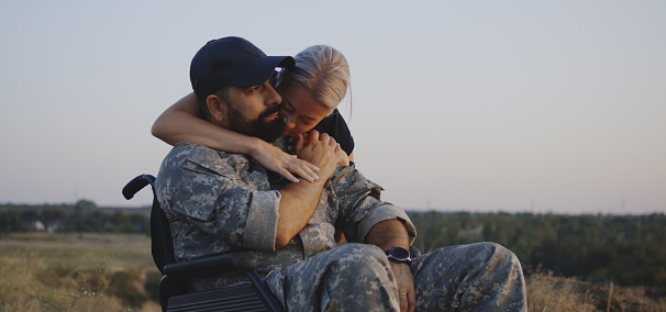 Medium shot of wife hugging wheelchaired soldier husband
