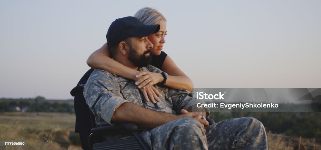 Wife hugging wheelchaired husband Medium shot of wife hugging wheelchaired soldier husband Veteran Stock Photo