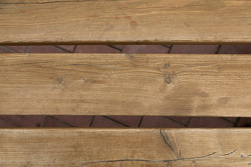 Close-up of light wooden panels with gaps against maroon street tile