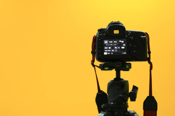 A back black camera on tripod shooting to yellow screen. A back black camera on tripod shooting to yellow screen blank copy space at left side. digital single lens reflex camera stock pictures, royalty-free photos & images