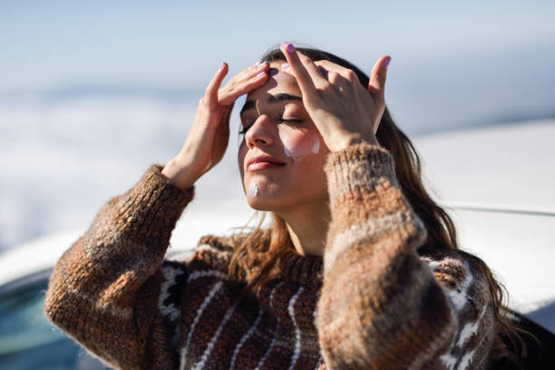 mujer joven aplicando protector solar en su rostro en el paisaje de nieve - crema de sol fotografías e imágenes de stock