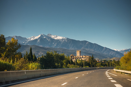Road accessing Vinca, a french village in Eastern Pyrenees and snow capped Canigou peak.