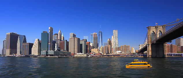 Lower Manhattan skyline, Eastern River and Brooklyn Bridge with a yellow water taxi boat on the foreground, New York City