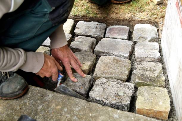 istock pavement works, Cobbled pavement natural stone. gloved Hands of worker installing concrete paver blocks with cement. a bricklayer laying paving stones carefully placing, with trowel putty knife 1177684336