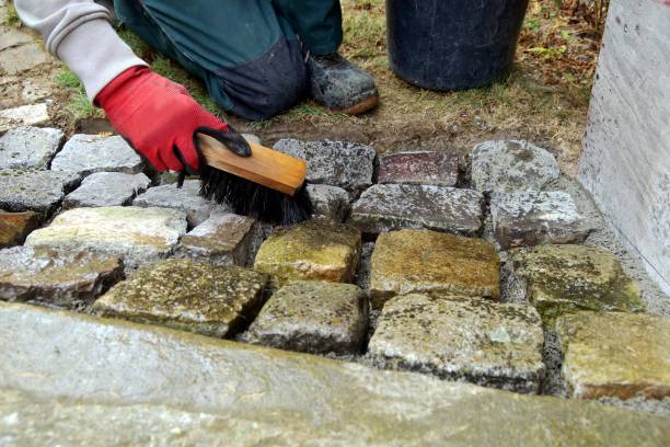 pavement works, Cobbled pavement natural stone. gloved Hands of worker cleaning concrete paver blocks with brush and water after laying paving stones carefully placing in cement stock photo