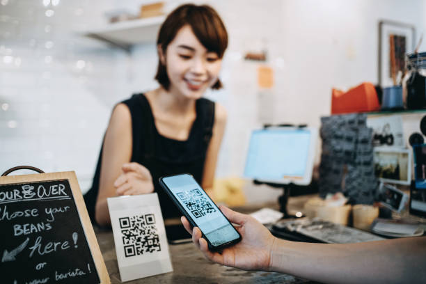 Customer scanning QR code, making a quick and easy contactless payment with her smartphone in a cafe in front of a smiling barista