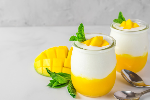 two glasses of mango yogurt with fresh fruits and mint over white concrete background. healthy breakfast. close up