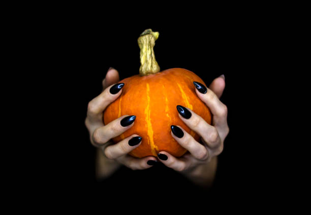 istock Happy Halloween theme. Witches knotty hands with black sharp long nails hold a small pumpkin, low key, selected focus. 1177706897