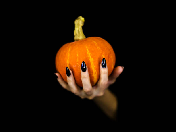 istock Witches knotty fingers with black sharp glossy nails hold a small pumpkin, low key, selected focus. 1177707449