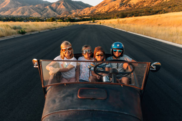 Two young boys and a two young girls in retro racing helmets and glasses are ready to drive in their antique Model T Ford car. These next generation racers represent the revival of classic vintage cars and are ready to escape to freedom. Photograph taken in Utah, USA.