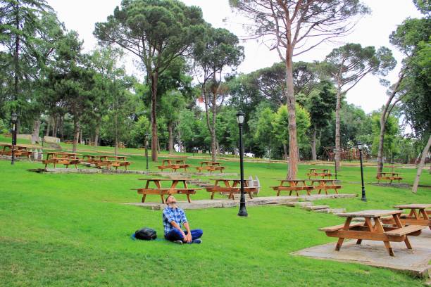 istock Man with backpack sitting on the grass with benches and trees background 1177712320