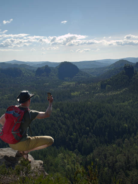 istock Hiking man with backpack, hat and phone sit on mountain cliff 1177716141