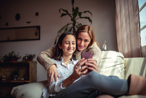 Mother and daughter sitting on a couch at home using a smartphone