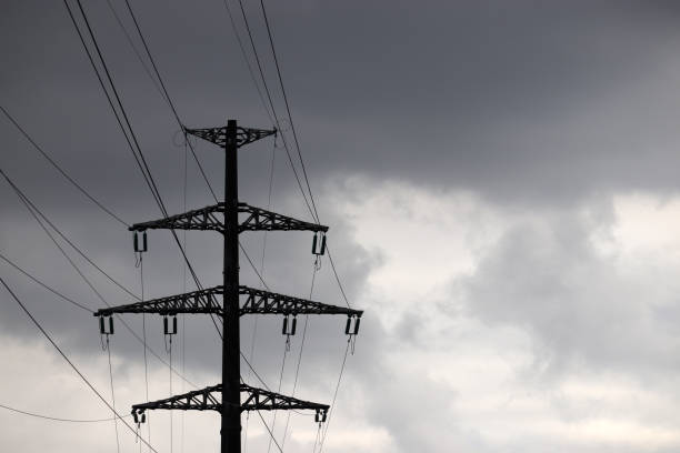 High voltage tower silhouette with electrical wires on storm sky background with dark clouds
