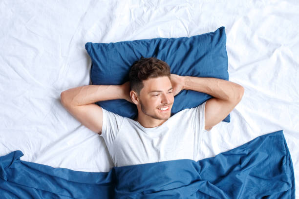 istock Bedtime. Guy lying on bed top view hands under head looking aside dreamful 1177724393