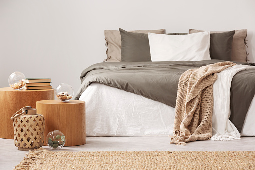 Mesa de noche de madera junto a cama king size con ropa de cama blanca y gris en interior de dormitorio sencillo photo