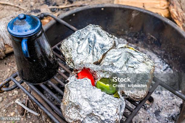 Blue Tea Water Kettle And Foil Wrapped Red Green Pepper Vegetables On Grill In Fire Pit At Campground Cooking Dinner Stock Photo - Download Image Now
