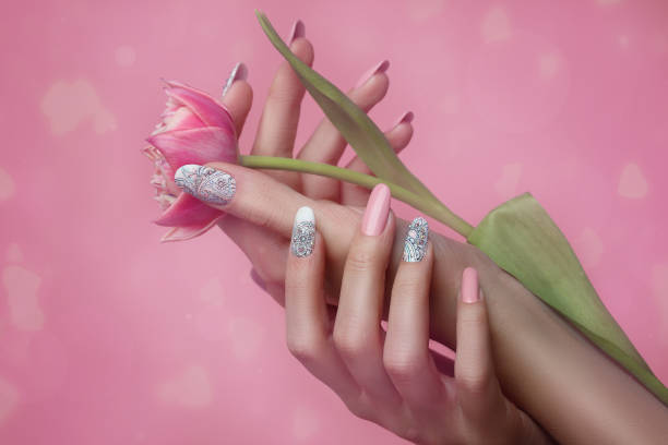 ネイルズアートデザイン。ピンクの背景にピンクのマニキュアと手。春の花とトレンディなピンクの爪で女性の手のクローズアップ。