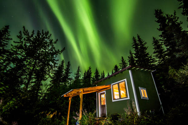 Bright green Aurora Borealis over small green and white tiny house in Alaska. A small house on a homestead in Alaska lit by headlamp under bright green Aurora borealis. The Northern lights illuminate the cold Alaskan autumn night. tiny house stock pictures, royalty-free photos & images