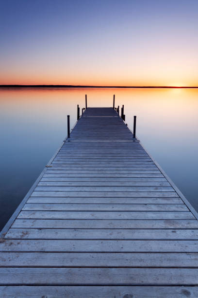 Dock pointing towards a sunset with a  still calm lake at Prince Albert National Park, Saskatchewan, Canada. Image taken from a tripod