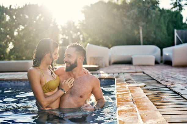 Affectionate couple standing in swimming pool Affectionate couple standing in swimming pool. Smiling man and woman relaxing in yard during weekend. They spending leisure time together. male swimsuit standing arm around stock pictures, royalty-free photos & images