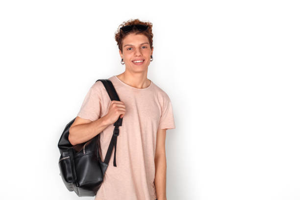 Teenager boy wearing earrings carrying backpack studio standing isolated on white wall looking camera smiling happy