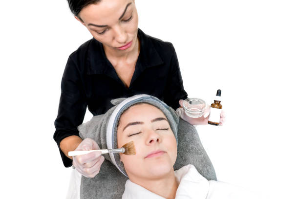Cosmetologist administering chemical peel treatment on patient in a beauty spa, for skin rejuvenation, complexion and acne beauty treatments. Two females in a clinical spa. Cosmetologist administering chemical peel treatment on patient in a beauty spa, for skin rejuvenation, complexion and acne beauty treatments. Two females in a clinical spa. facial chemical peel stock pictures, royalty-free photos & images