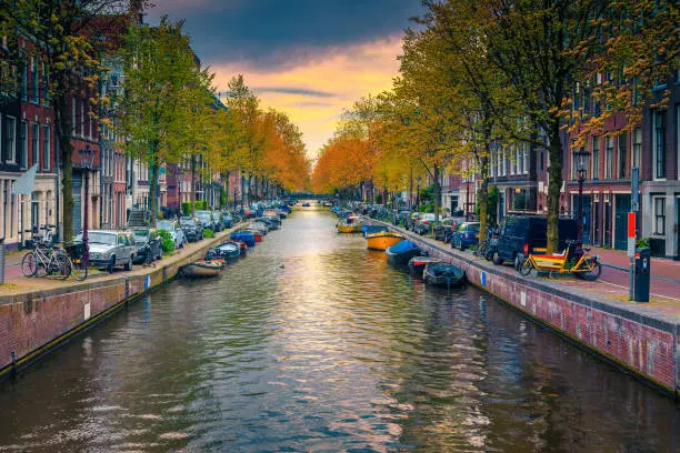 Photo of Narrow water canal with boats at sunset in Amsterdam, Netherlands