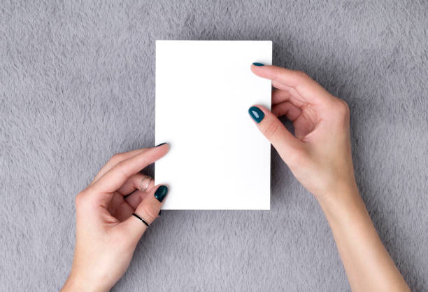 Manicured woman's hands holding postcard on grey furry background. Plain call-card mock up template.