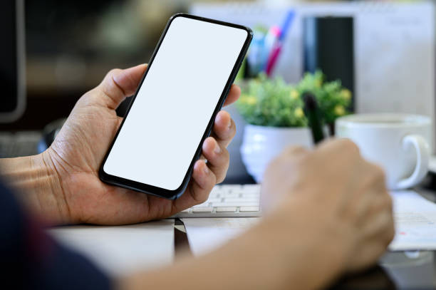 istock Closeup man hand holding smartphone with blank white screen while working at office desk. 1177816452