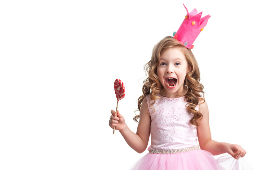 Beautiful little candy princess girl in crown holding big pink heart lollipop and screaming isolated on white