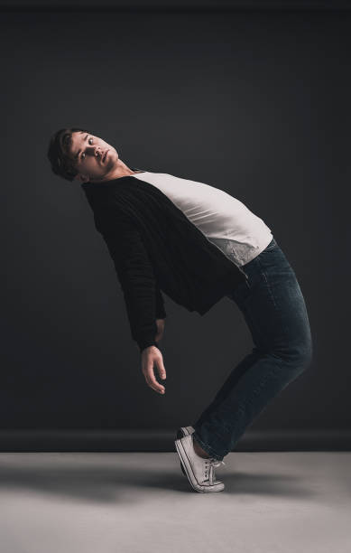 istock Young stylish man posing and dancing in the studio on a gray background. Dressed in a white T-shirt, blue jeans, black jacket and white sneakers. Model tests for men. 1177816765